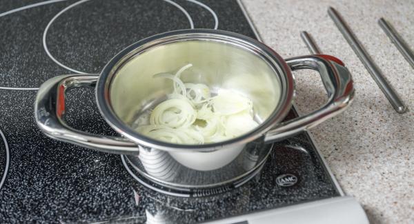 Mientras tanto, pelar la cebolla, cortarla por la mitad y después en rodajas finas. Introducirla en una olla pequeña o una sartén, tapar y colocarla en el fuego a temperatura máxima. Encender el Avisador (Audiotherm), colocarlo en el pomo (Visiotherm) y girar hasta que se muestre el símbolo de “chuleta”.