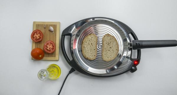Reducir a baja temperatura, colocar las 2 rebanadas de pan en la oPan y asar por un lado. Dar la vuelta y frotar el pan con el tomate y el ajo.