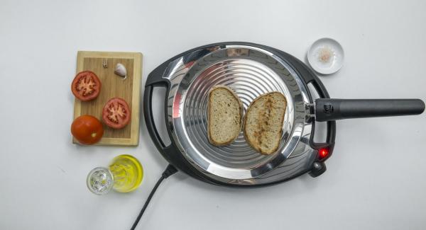 Reducir a baja temperatura, colocar las 2 rebanadas de pan en la oPan y asar por un lado. Dar la vuelta y frotar el pan con el tomate y el ajo.
