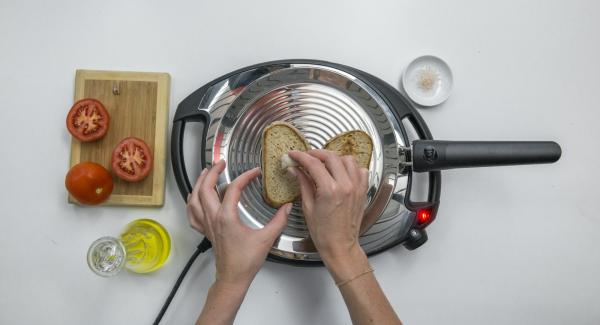 Reducir a baja temperatura, colocar las 2 rebanadas de pan en la oPan y asar por un lado. Dar la vuelta y frotar el pan con el tomate y el ajo.