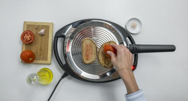 Reducir a baja temperatura, colocar las 2 rebanadas de pan en la oPan y asar por un lado. Dar la vuelta y frotar el pan con el tomate y el ajo.