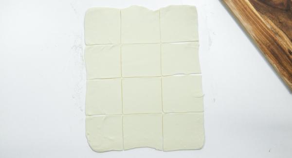 Extender la masa de hojaldre sobre una superficie de trabajo enharinada y cortarla en doce cuadrados de 10 x 10 cm.