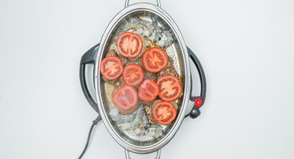 En cuanto se alcance la temperatura de 90 °C, girar los filetes y colocar 1 rodaja de tomate sobre cada filete. Añadir las gambas en los extremos.
