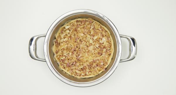 Colocar el papel de hornear en la olla, engrasar un poco el fondo de la olla. Extender la masa en Ø 26 cm y colocarla en la olla haciendo un pequeño borde. Añadir la mezcla de cebolla y la de huevos. Espolvorear con semillas de alcaravea.