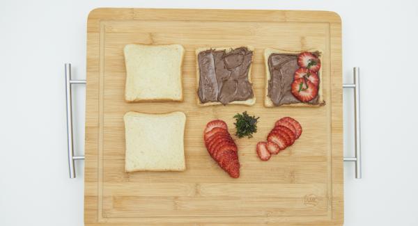 Untar dos rebanadas de pan tostado la crema de chocolate y avellanas. Limpiar las fresas y cortar en lonchas finas. Picar finamente las hojas de menta y espolvorear un poco en la tostada.